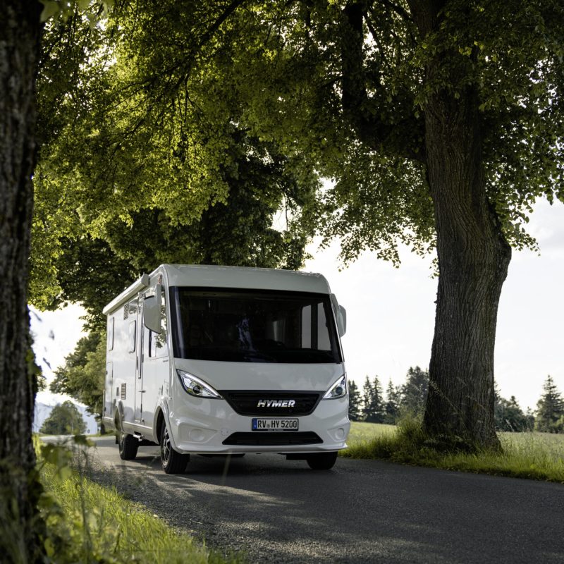 Kamper Hymer Exsis-I na drodze, otoczony drzewami.